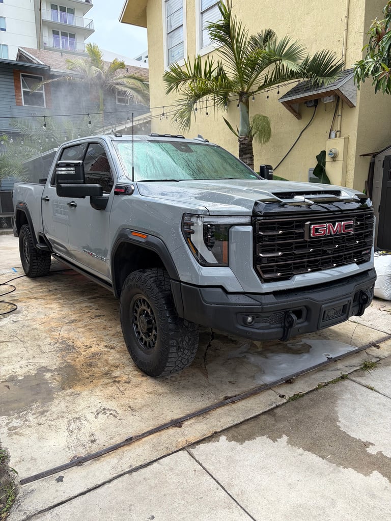 White GMC Sierra pickup truck parked in a driveway with palm trees and residential buildings in the background