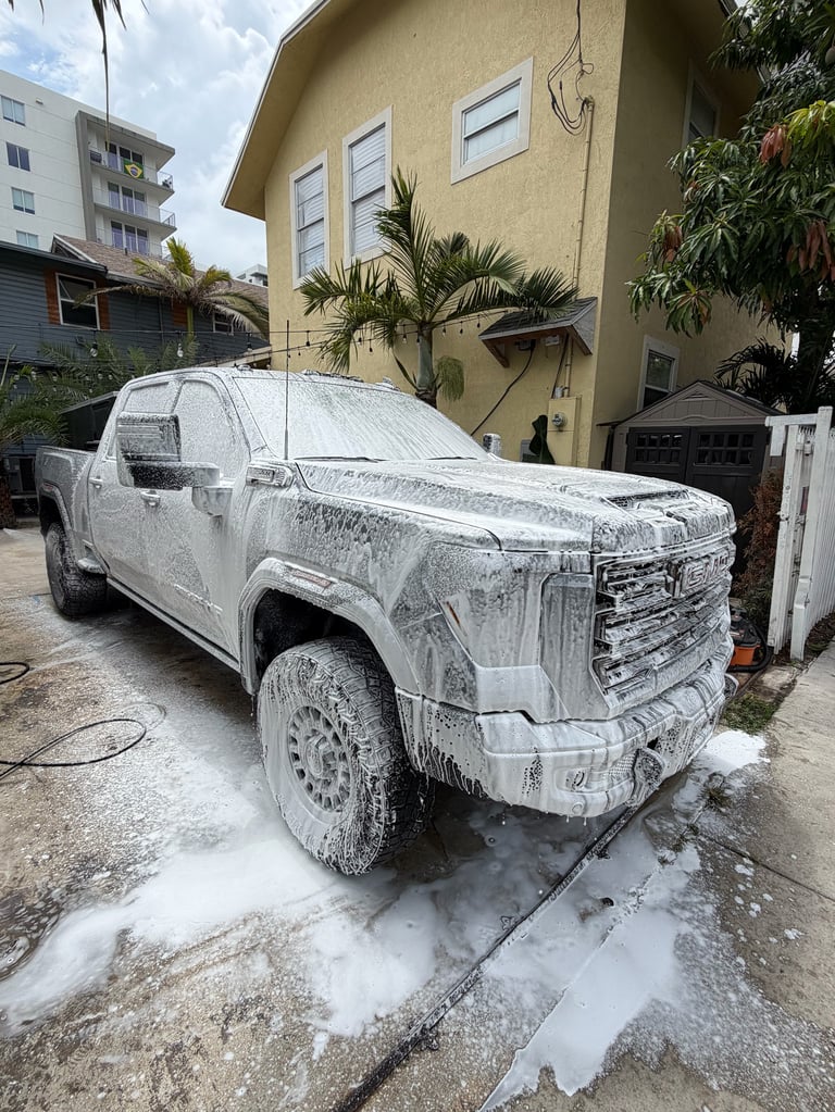White pickup truck being washed with soap and water in a residential driveway on a sunny day